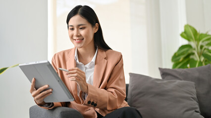 Attractive Asian businesswoman sitting on sofa, using her portable digital tablet.