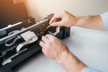 Maintenance and repair of printers. Master's hands with screwdriver. Background. Urgent repair of...