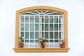 Glass window decorated with flowers on the outside. Yellow framed window in white wall, view from outside.