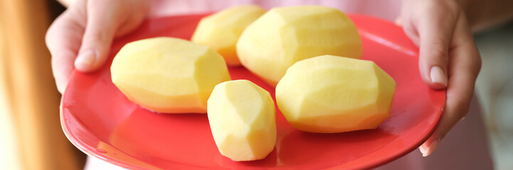 Female hands holding plate with raw peeled potatoes on it