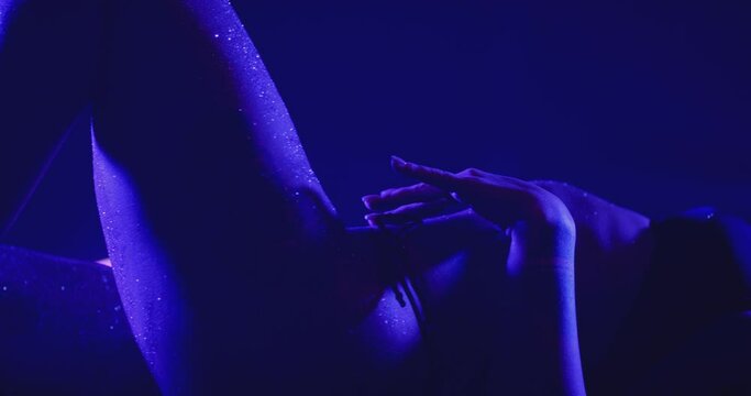 Closeup view of beautiful sexy woman dancing, posing and flirting inside dark place. Sensual scene of female model doing different sexy movements . Female model with g-string and tattoos in strip club