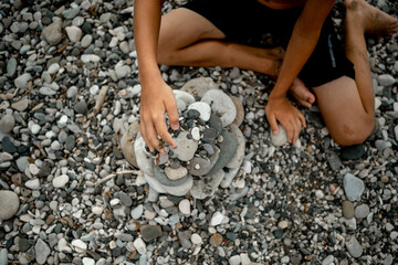 A boy on the beach builds a tower of stones