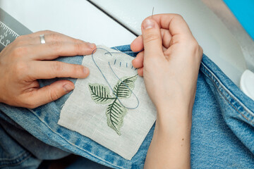 A woman mends jeans, sews a patch on a hole, hands close-up.Mending clothes concept,reusing old jeans. - obrazy, fototapety, plakaty