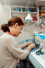 A woman mends jeans,sews a patch on a sewing machine in the home studio.Mending clothes...