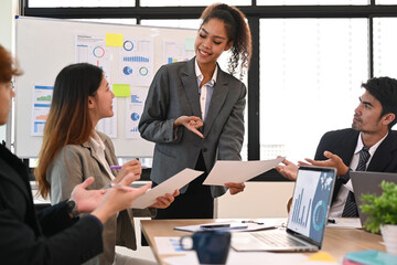 Smiling African American project manager giving presentation on flip chart to diverse corporate team at office meeting