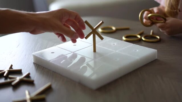 Close-up of adult and child play tic-tac-toe made of metal and stone