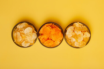 Crispy potato chips in a glass dark transparent bowls from above on yellow background