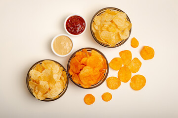 Paprika flavored potato chips and original chips with salt in small glass bowls, two kind of sauces from above on a light beige background. Snacks for group of people.