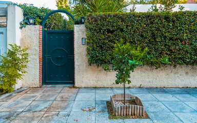 A family house exterior with a green door and fence by the sidewalk. Athens, Greece.