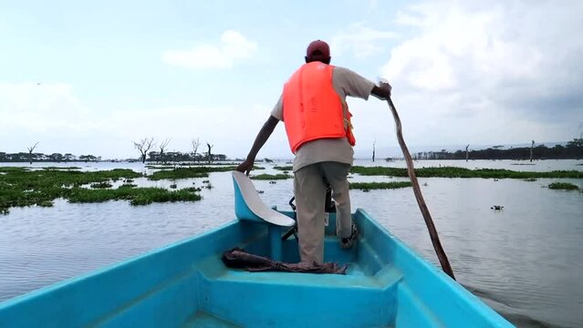 African man rowing with a stick in a blue fiber boat leaving Crescent Island, Kenya