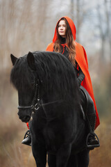 Beautiful girl in red cloak on black stallion