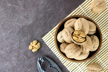 Walnut kernels, whole walnuts in a wooden bowl and a nutcracker on a brown background. Nuts on a dark background. Top view, copy space.