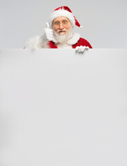 Handsome Santa Claus in glasses and white gloves holds a large vertical blank board and looks at the camera. Big white banner with Santa Claus showing thumbs up.