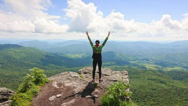 Back view of glad female tourist climbing hill, achieving goal. Young, happy, glad woman hiking in mountains, running, jumping, raising hands. Concept of traveling and hiking.