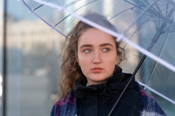 Portrait of young woman with lush long brown hair under transparent umbrella. Look on side....