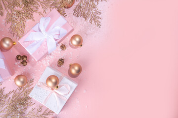 Rose gold Christmas, New Year background with golden christmas tree twigs and balls, holiday gift boxes, decorations, artificial snow, flat lay on pink background copy space