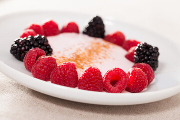 raspberries and blackberries laid out on a white plate in circle with yogurt and cinnamon