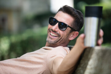man sitting on a bench with tablet and drinking coffee