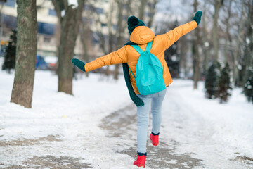 Rear back behind view of preteen girl wearing warm clothes dancing having fun wintertime snowy weather outdoors