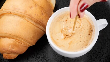 French baked croissant and cup of coffee. Putting sugar in coffee cup and stirring
