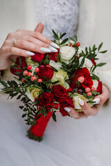 Bride holds wedding bouquet with red roses in hand, showing her manicure