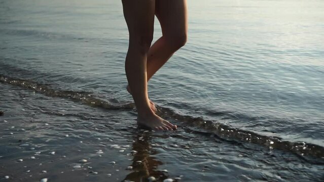 Female legs or feet walking in sea water, sunrise morning view, detail slow motion