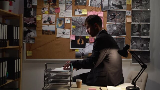 Detective looking at evidence board with photos in office, working at night