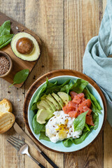 Delicious breakfast or lunch bowl with salted salmon fish, avocado, boiled egg and spinach on a rustic table. Ketogenic, keto or paleo diet. View from above. Copy space.