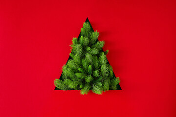 Christmas tree silhouette made of fir branches on red background. Flat lay. New Year minimal...