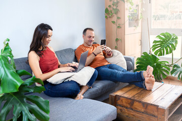 couple sitting on sofa with laptop and phone