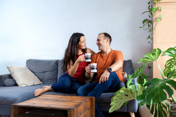 couple sitting on the sofa smiling while drinking coffee