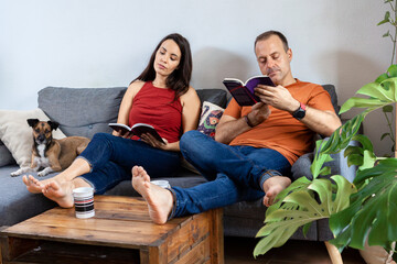Couple and dog sitting on sofa and reading books 