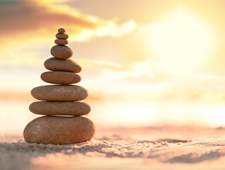 Balanced pebble pyramid on the beach. Abstract warm sunset bokeh with sand on the background. Zen stones on the sea beach.