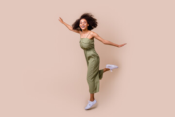 Full body photo of pretty young woman wavy hair jump spread hands plane pose dressed stylish khaki look isolated on beige color background