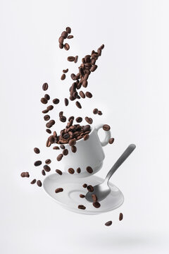 roasted coffee beans spilled from a floating cup and a teaspoon isolated on white background