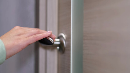 side view of a woman enters a bright room, takes the first step. Close-up of a female hand opening a white door with a metal handle.