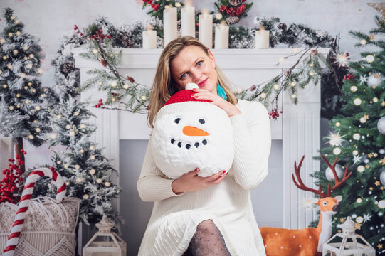 Girl with snowman cushion festive Christmas decoration background white dress bright studio picture 