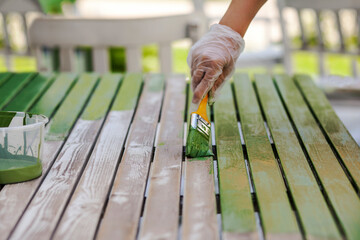 Painting Table with brush in protective gloves. Worker Paints garden Wood furniture in green. Renewing, Renovation Wooden Garden Furniture