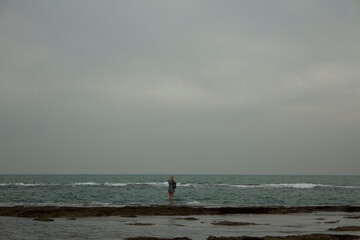 Fototapeta na wymiar blonde woman in a short dress walking above the sea looking at her reflection in the water on a cloudy day in the bay of Cadiz.