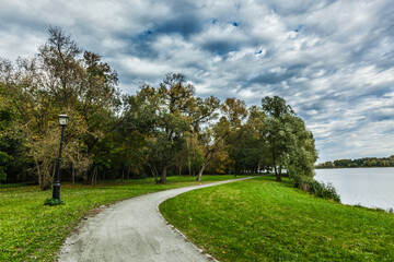Path in autumn park near the lake with dramatic sky