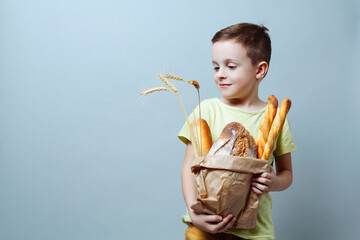child with a grocery bag with freshly baked bread and ears of wheat, smiling softly against a uniform background.