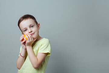 child with tangerine in his hands smiling softly and gently presses it to the face