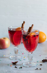 Two glasses of mulled wine, spices, fruits, small snowflakes on light background
