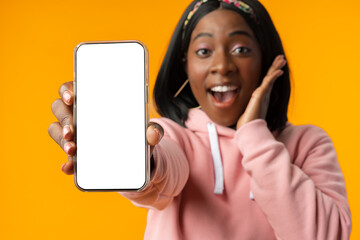Portrait of a excited young african woman showing blank screen mobile phone over yellow background