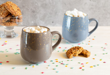 Two cups of cocoa with marshmallows and oatmeal cookies on a light background
