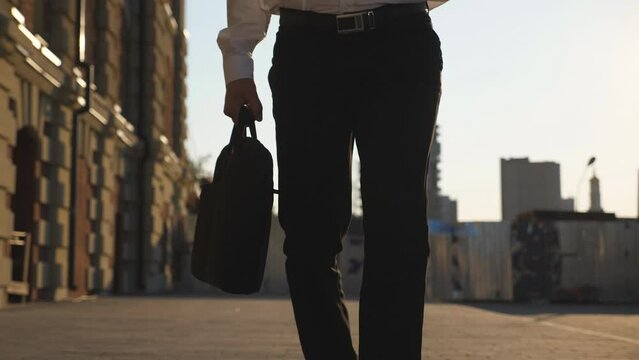 Male feet of entrepreneur in black shoes going on sidewalk. Legs of office worker stepping to work. Businessman with briefcase walking to job at urban street. Business and finance concept. Dolly shot