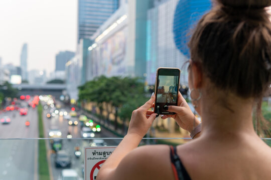 Unrecognizable young woman taking a picture of a large city avenue with the lights of billboards and cars.