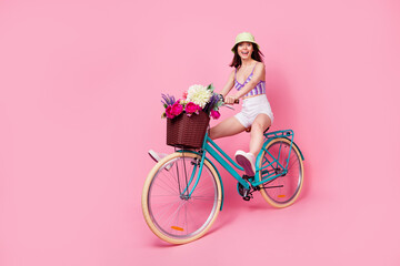 Full length photo of excited funky girl dressed violet top having fun driving bike empty space isolated pink color background