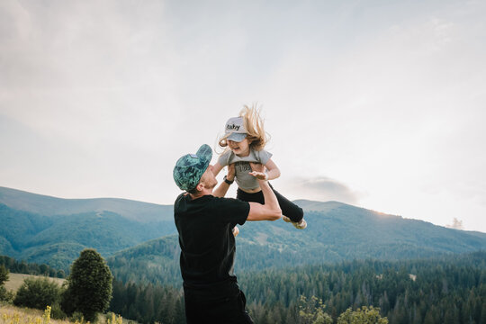 Portrait of father throws up happy daughter on hands, walking on nature in autumn day. Dad and child playing in the mountains. Concept of family spending time together on vacation. World Tourism Day.