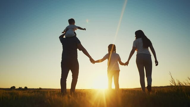 people in the park. happy family walking silhouette at sunset. mom dad and daughters walk holding hands in the park. happy sun family childhood dream concept. parents and children go back silhouette